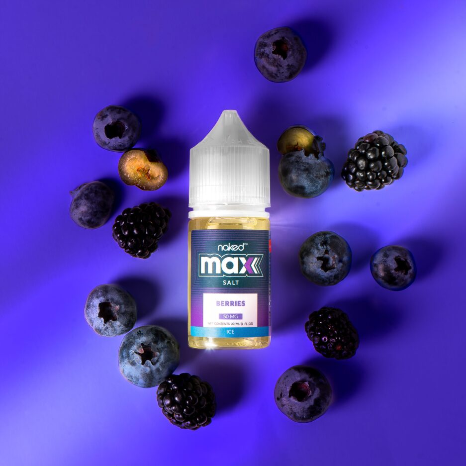 A top down shot with MAX's Berries at the center illuminated by a light off to the left of the image outside of frame, surrounding the bottles are its ingredients which is blueberries and blackberries.