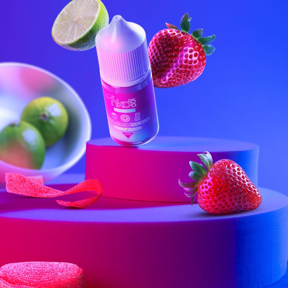 On two layered platforms, strawberries, limes, and sour belt candy are staggered and illuminated by two neon lights on the sides of the image outside of the view. Strawberry Sour Candy is standing and angled on the top platform.