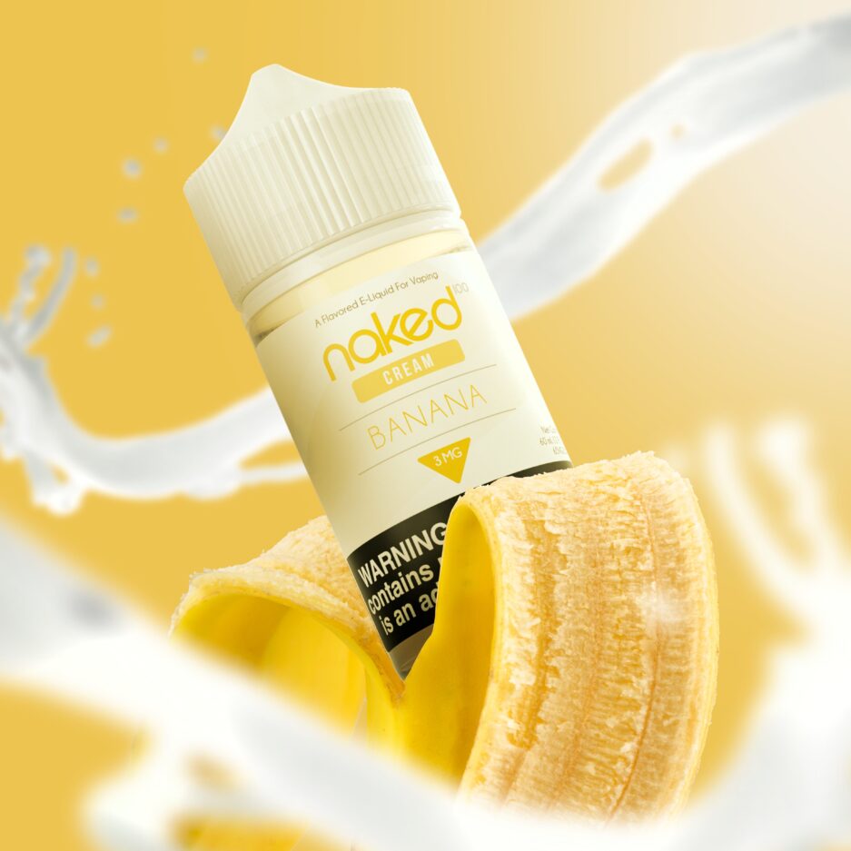 Splashes of cream are blurred in the foreground and background, with Naked100's Banana sitting inside a banana peel at the center of the image.