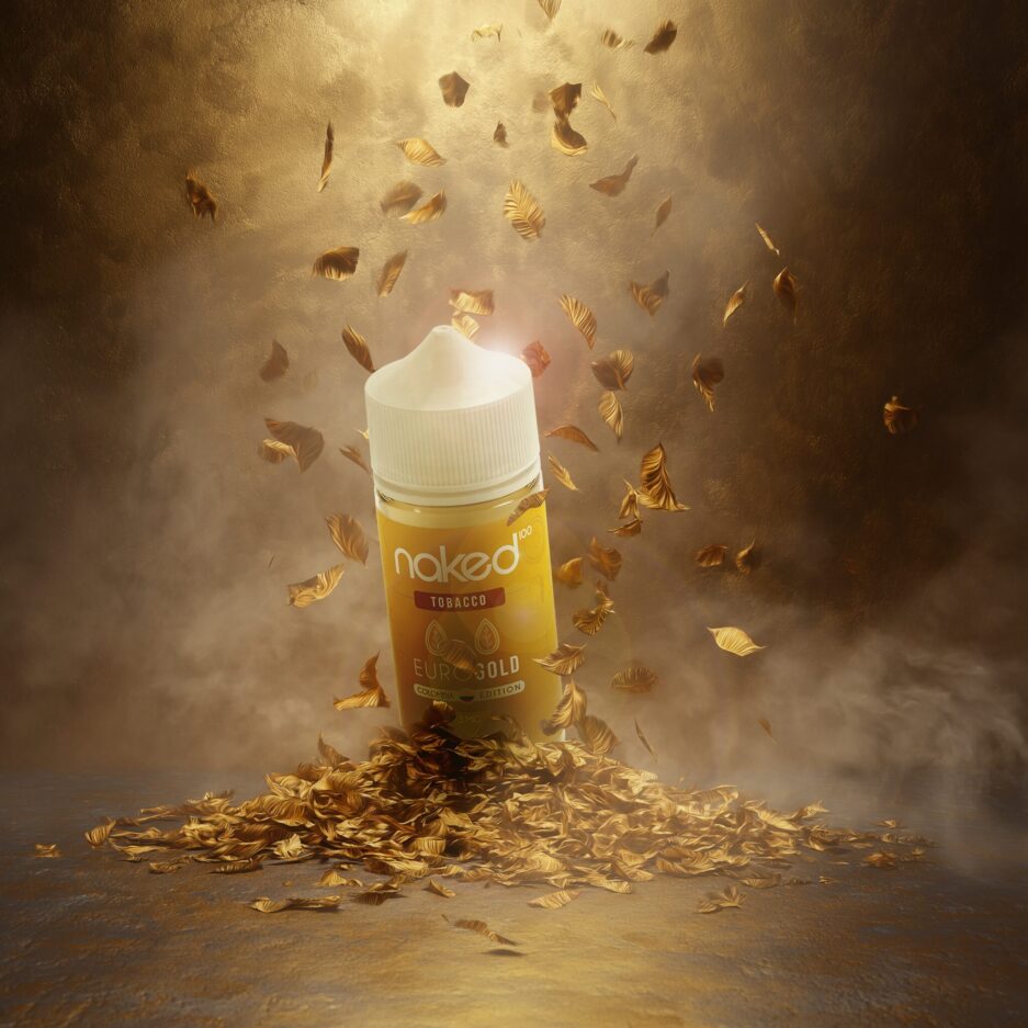 A product set with dramatic lighting, one large light from above illuminating the center of the image. The floor and walls are gold colored with gold tobacco leafs piled onto the center of the floor with more leafs falling from above. Naked 100 Colombia's Euro Gold sits on top of the pile with the front label partially dark and light seeping from the back and sides of the bottle. Light smoke is dissipating throughout the image.