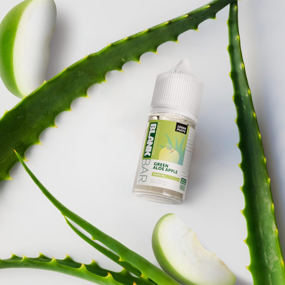 A top down shot with a white mate floor, Apple slices spread out along with aloe plant stems laid out, with Green Aloe Apple at the center.