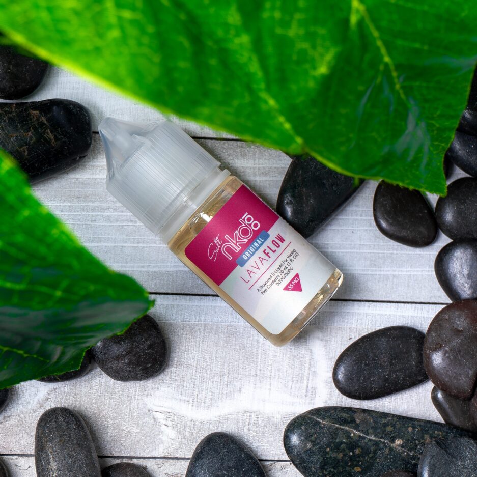 Lava Flow laying on a white wood floor, camera angle is top down. Lava rocks are scattered around the bottle, with leafs peering from the top side.