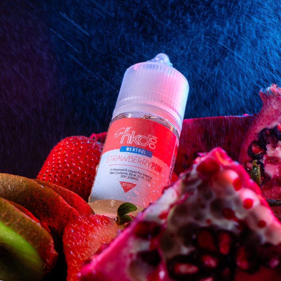 Set in dramatic lighting, with heavy rain falling and a neon red light illuminating the area along with a blue neon light partially illuminating from behind, Strawberry Pom Salt sits angled on a pile of pomegranates, kiwis, and strawberries.