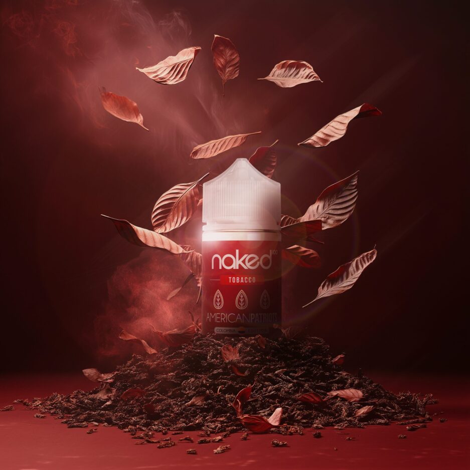 A product shot with red and burgundy color tones, matte floor and seamless background, a pile of tobacco at the center with tobacco leafs falling towards the center from the top, Naked100 Colombia's American Patriots sits in the center partially dug into the tobacco, with light from the top partially illuminating the bottle. Minimal smoke comes from the tobacco on the floor rising in the air.