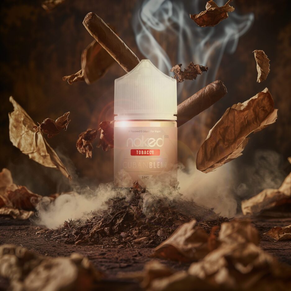 A product shot setup in a dramatic brown and tan colored tone aesthetic with tobacco piled in the middle of the image, tobacco leafs floating towards the middle of the image and in the foreground blurred out, with smoke seeping from the back into the middle of the image. Naked 100's Cuban blend 60mL bottle sits in the middle of the image dig into the tobacco standing high with the smoke peering through the sides of the bottle. Cigars falling behind the bottle to give off the style of tobacco this product provides.