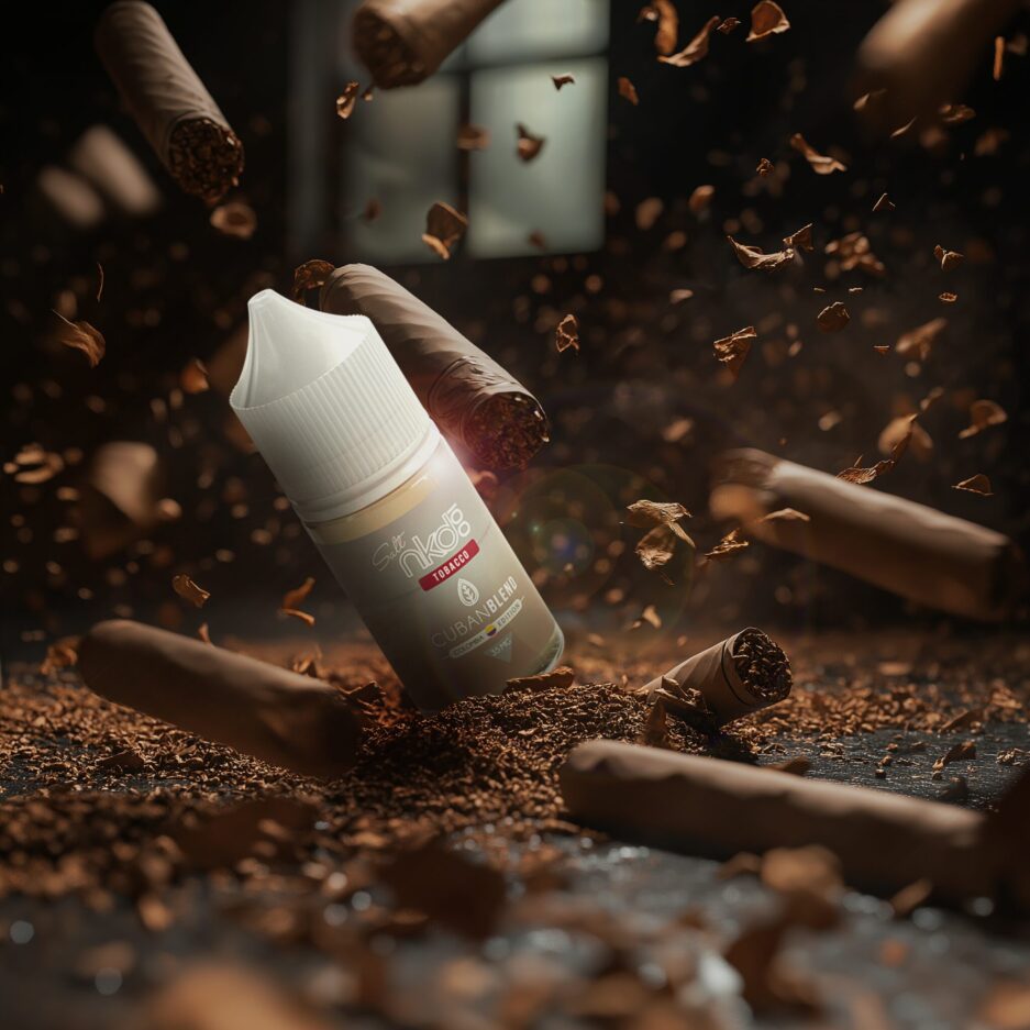 A dramatic product setup with a black concrete floor, tobacco piled into the center, tobacco shavings scattered around the whole image blurred and not, Cuban cigars are on the floor and falling from the sky. Naked100 Colombia's Cuban Blend lies on top of the tobacco pile showcases itself partially dug into the tobacco.